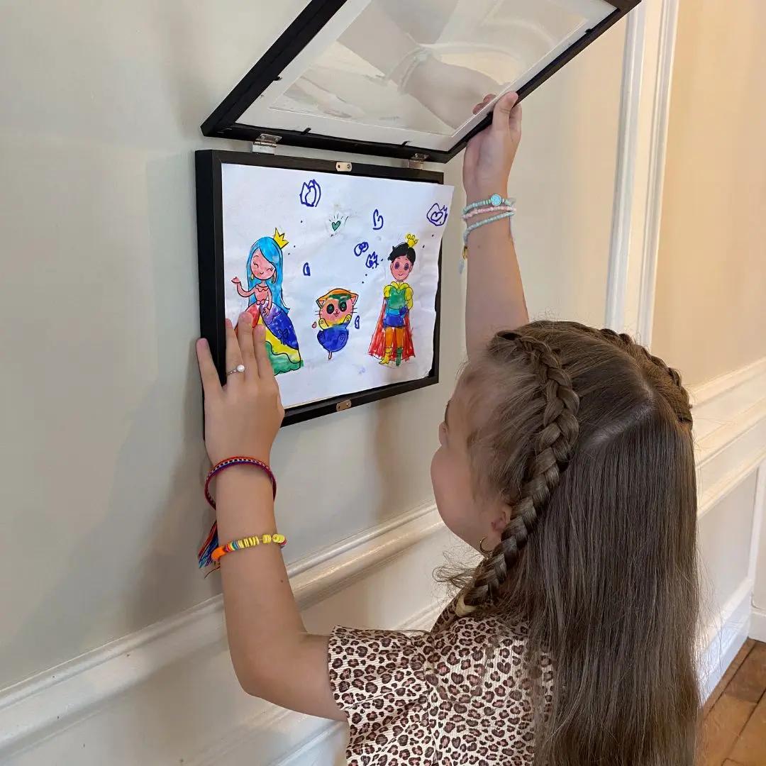 Enfant accrochant un cadre mural pour exposer ses dessins